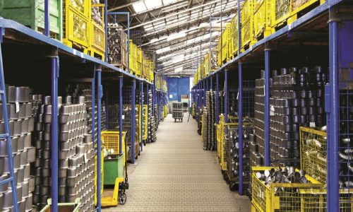 A spacious warehouse aisle lined with metal containers stored on blue and yellow shelves, showcasing industrial storage solutions.