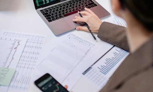 A business professional analyzing stock charts on a laptop and smartphone at the office.